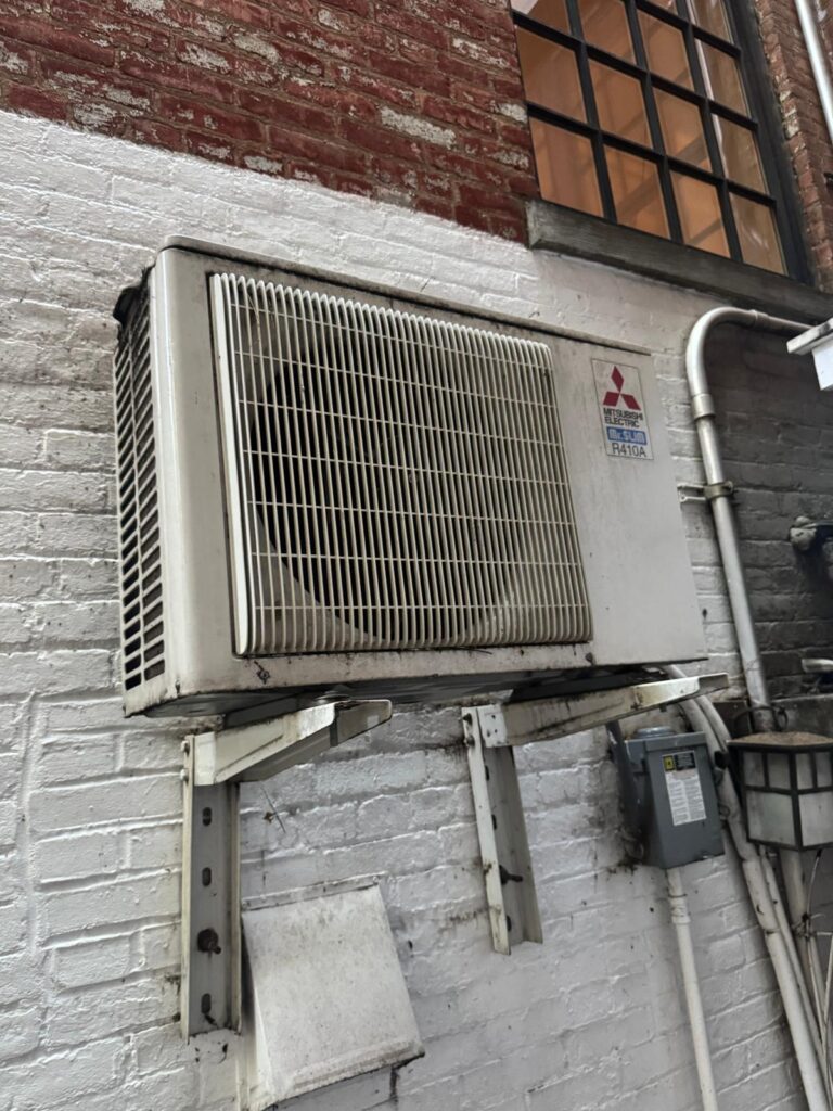 Mitsubishi ductless mini-split condenser mounted on an exterior brick wall